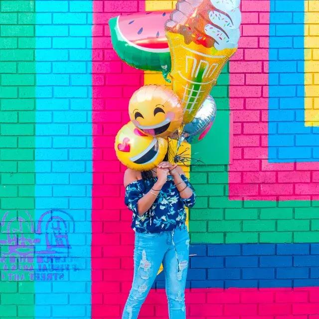 Une fille fête son anniversaire avec des ballons devant une fresque colorée.